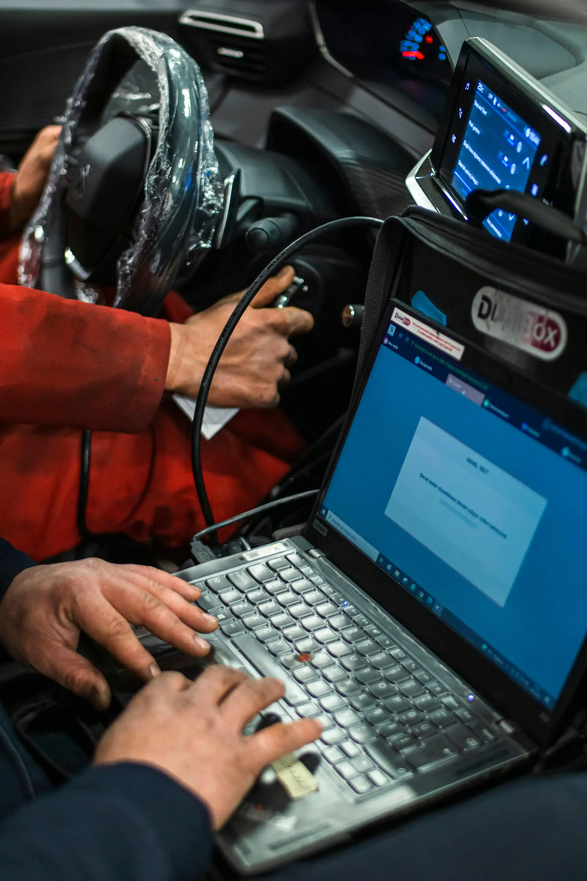A technician in a car running a diagnostic scan on a laptop