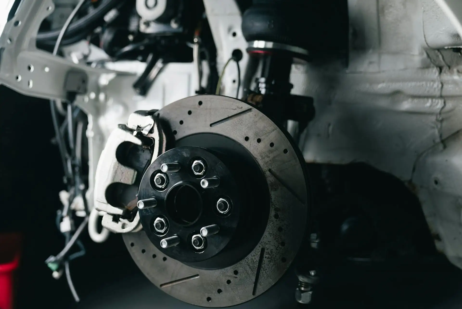 Close-up of a drilled brake disc and white caliper on a car up on a lift