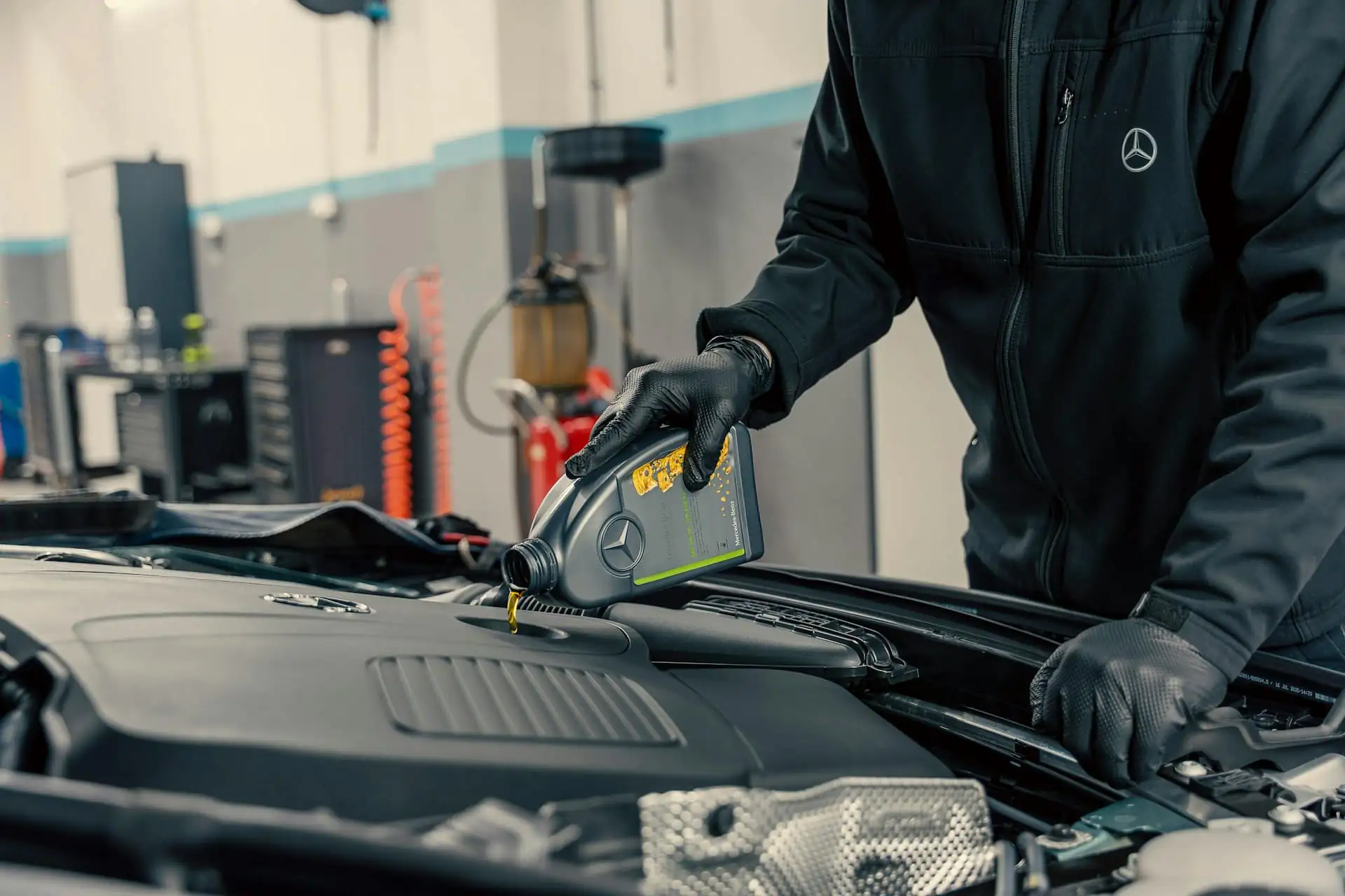 A mechanic in black gloves pouring engine oil into a car engine
