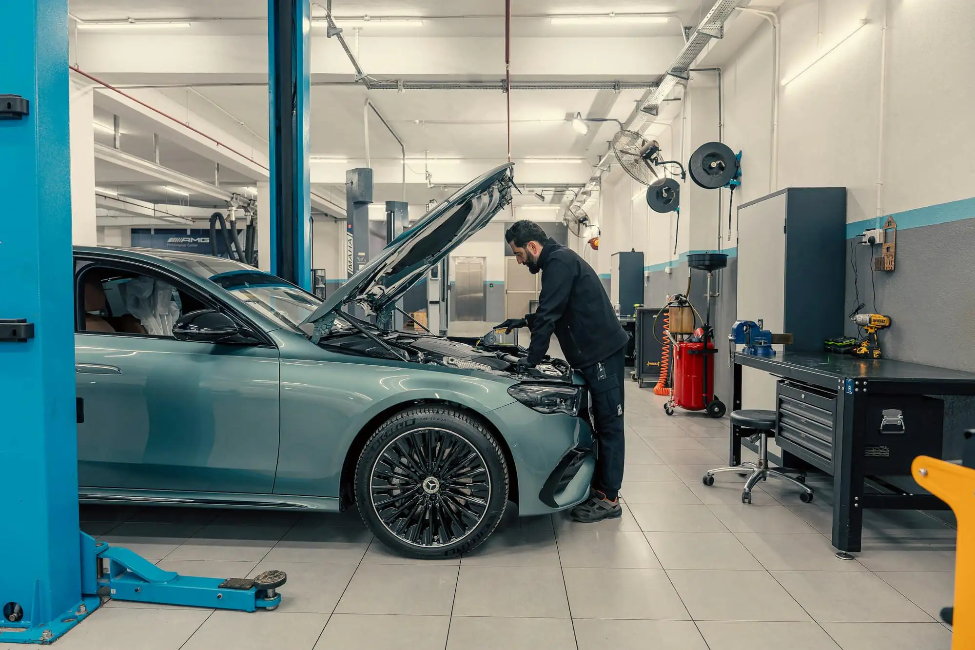 A mechanic working under the bonnet of a car raised on a lift in a bright workshop