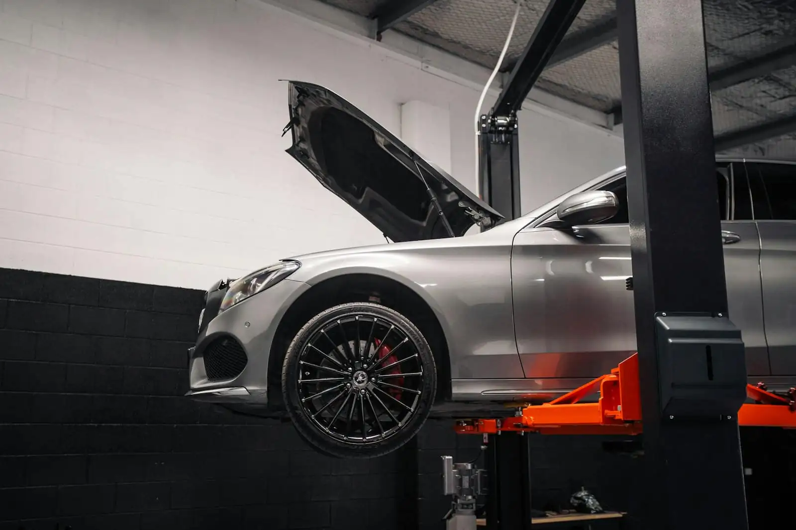 A silver car with its bonnet open on an orange hydraulic lift
