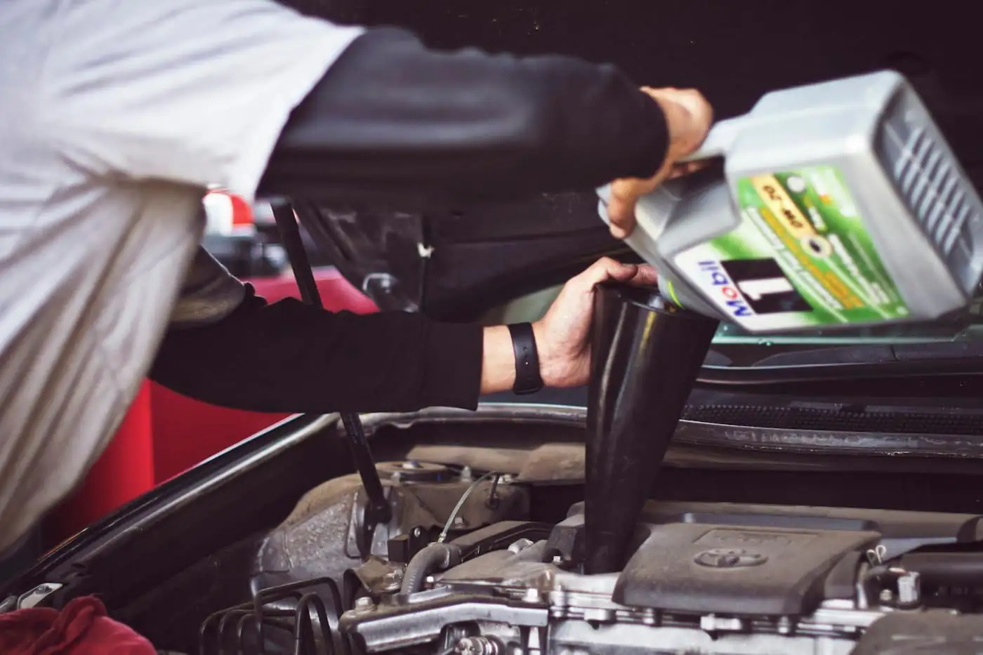 A mechanic refilling engine oil through a funnel